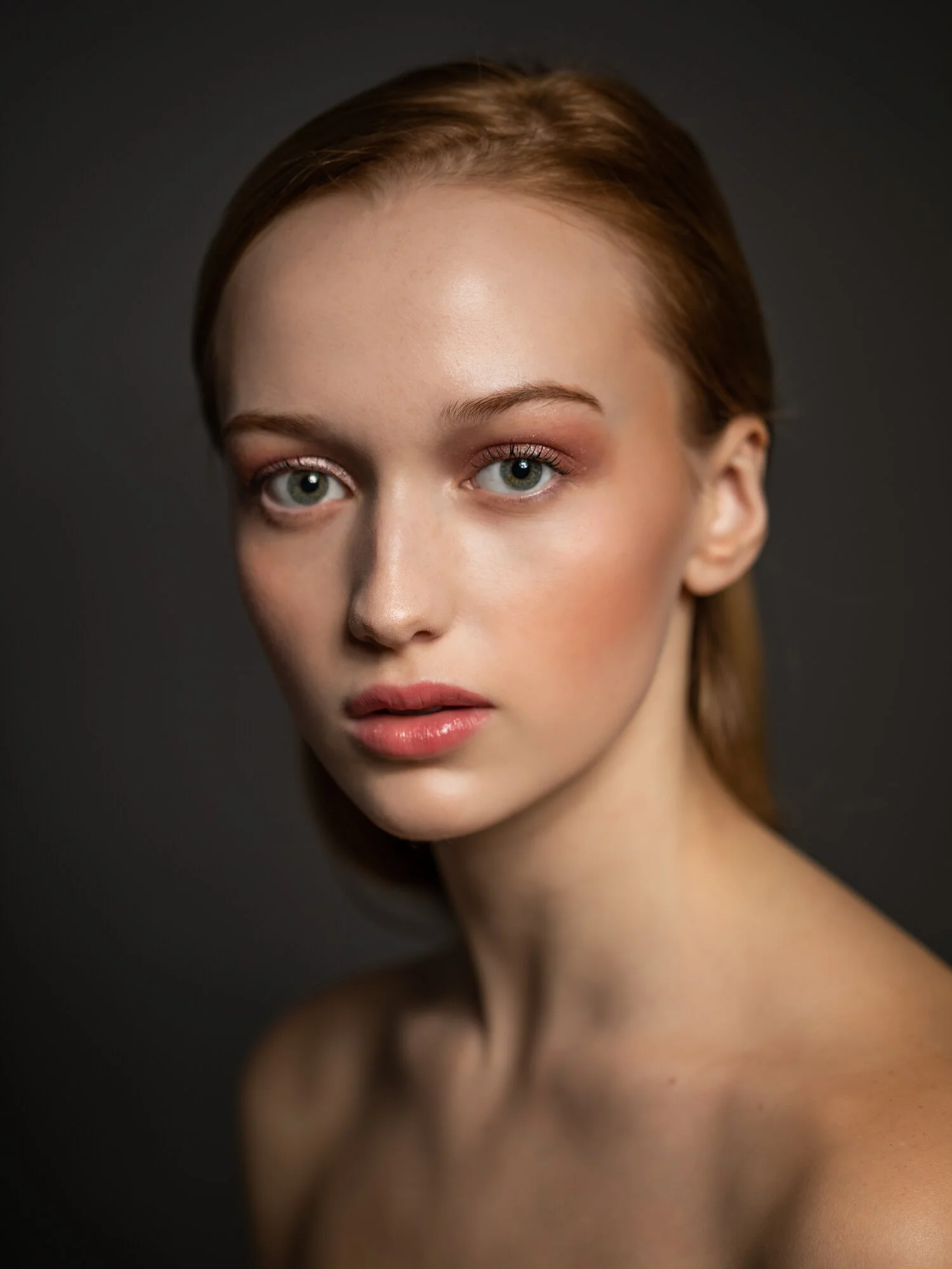 A portrait of a young woman with fair skin, light makeup, and red hair against a dark background.