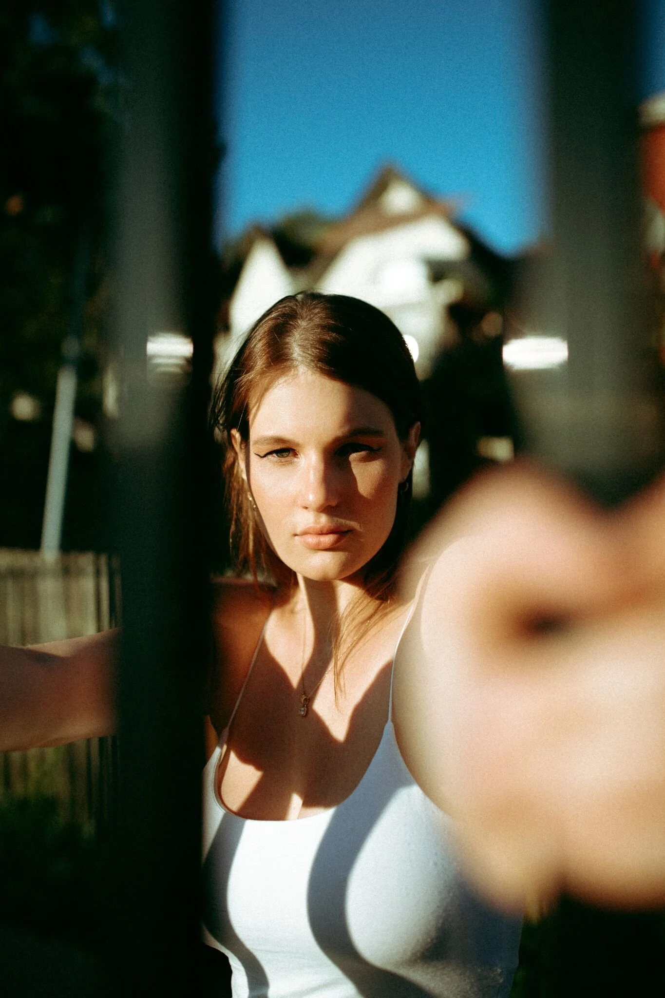 A woman with brown hair taking a selfie outdoors during sunset, with a house and a fence visible in the background.