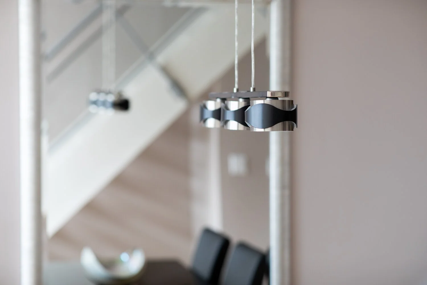 Modern pendant lights hanging from the ceiling above a dining table, with part of a staircase visible in the background.