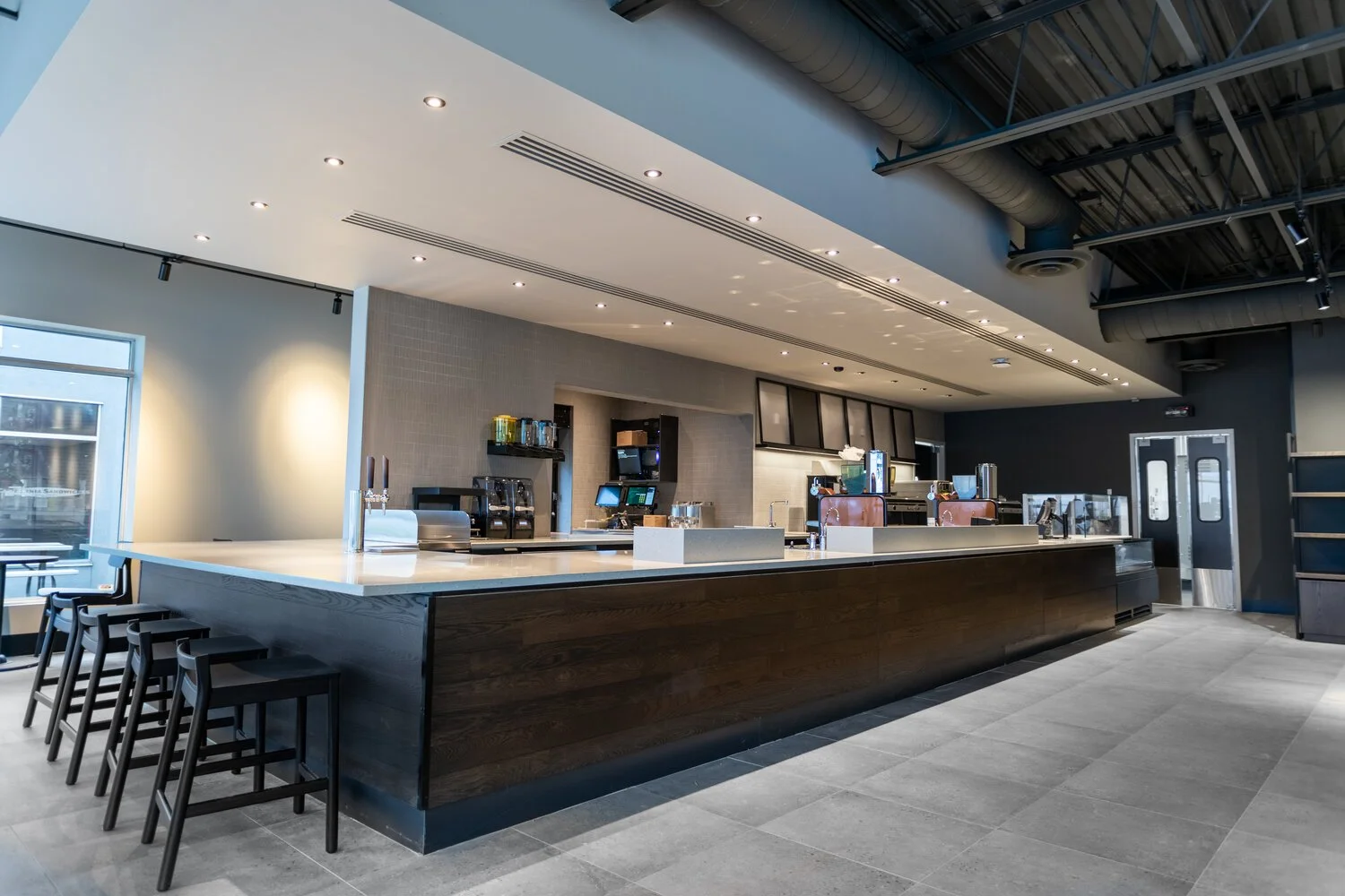 Modern, empty coffee shop or cafe counter with seating area, coffee machines, and digital order screens, featuring minimalistic design and neutral color palette.