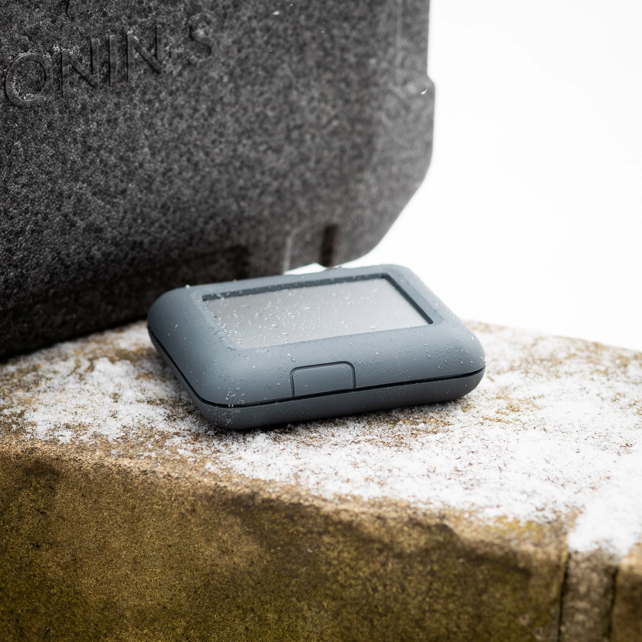 GPS device with water droplets on its screen resting on a snowy stone surface.