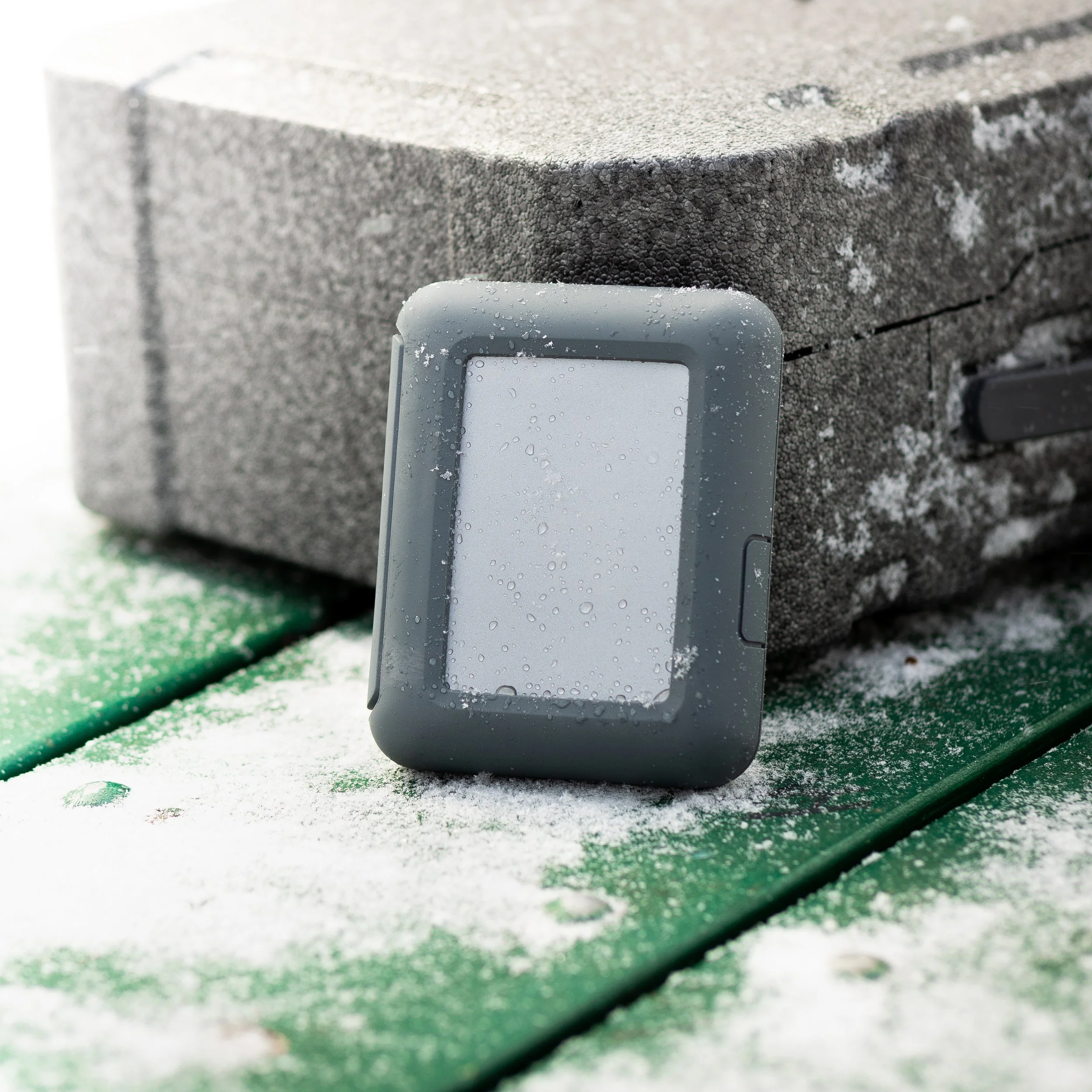 Smartwatch covered in water droplets resting on a snow-dusted bench.
