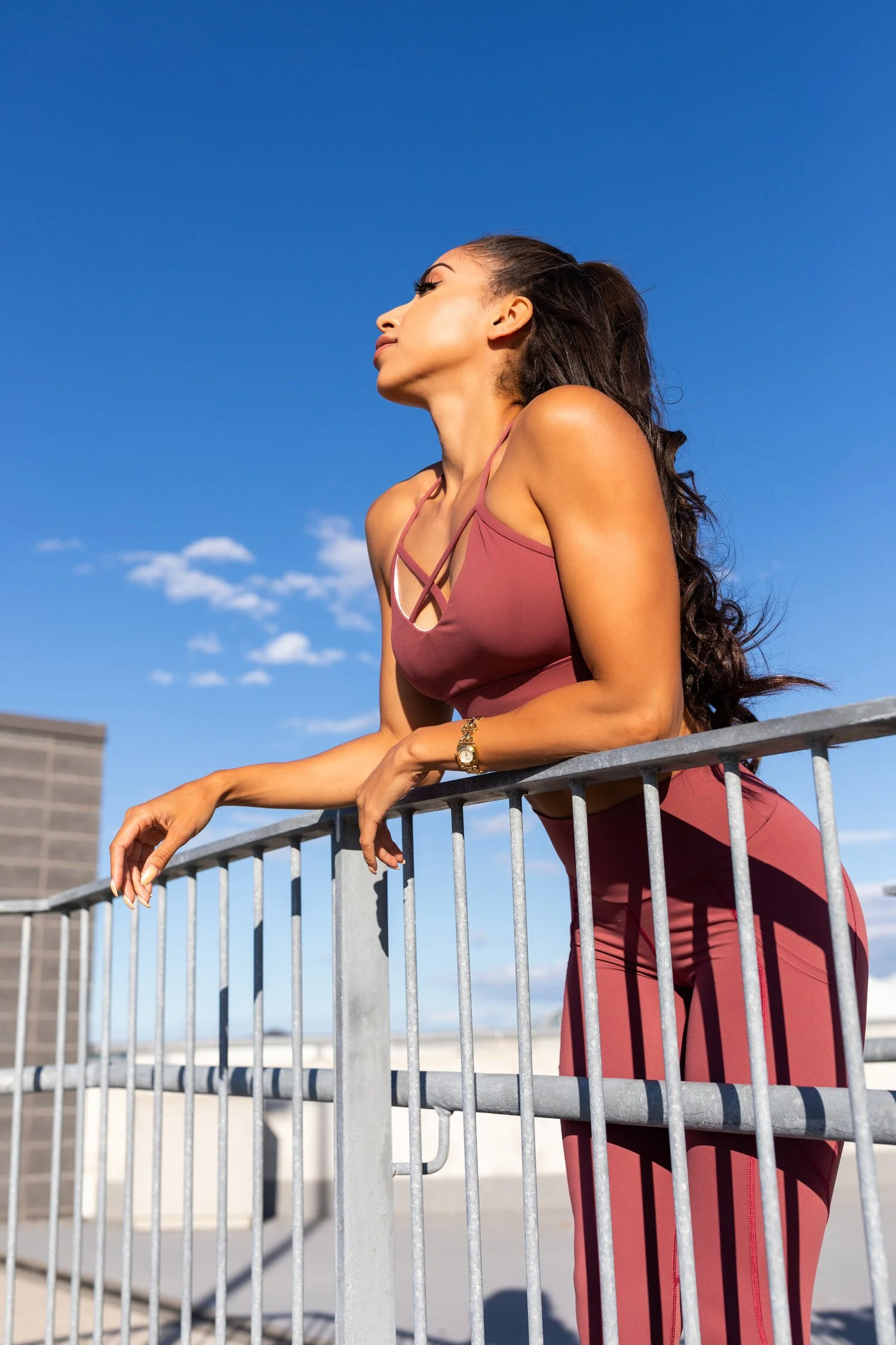 Woman in athletic wear leaning on a metal railing under a clear blue sky.