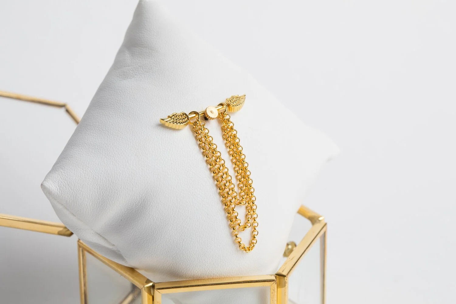 Gold layered chain necklace with wing and floral charms on a jewelry stand.