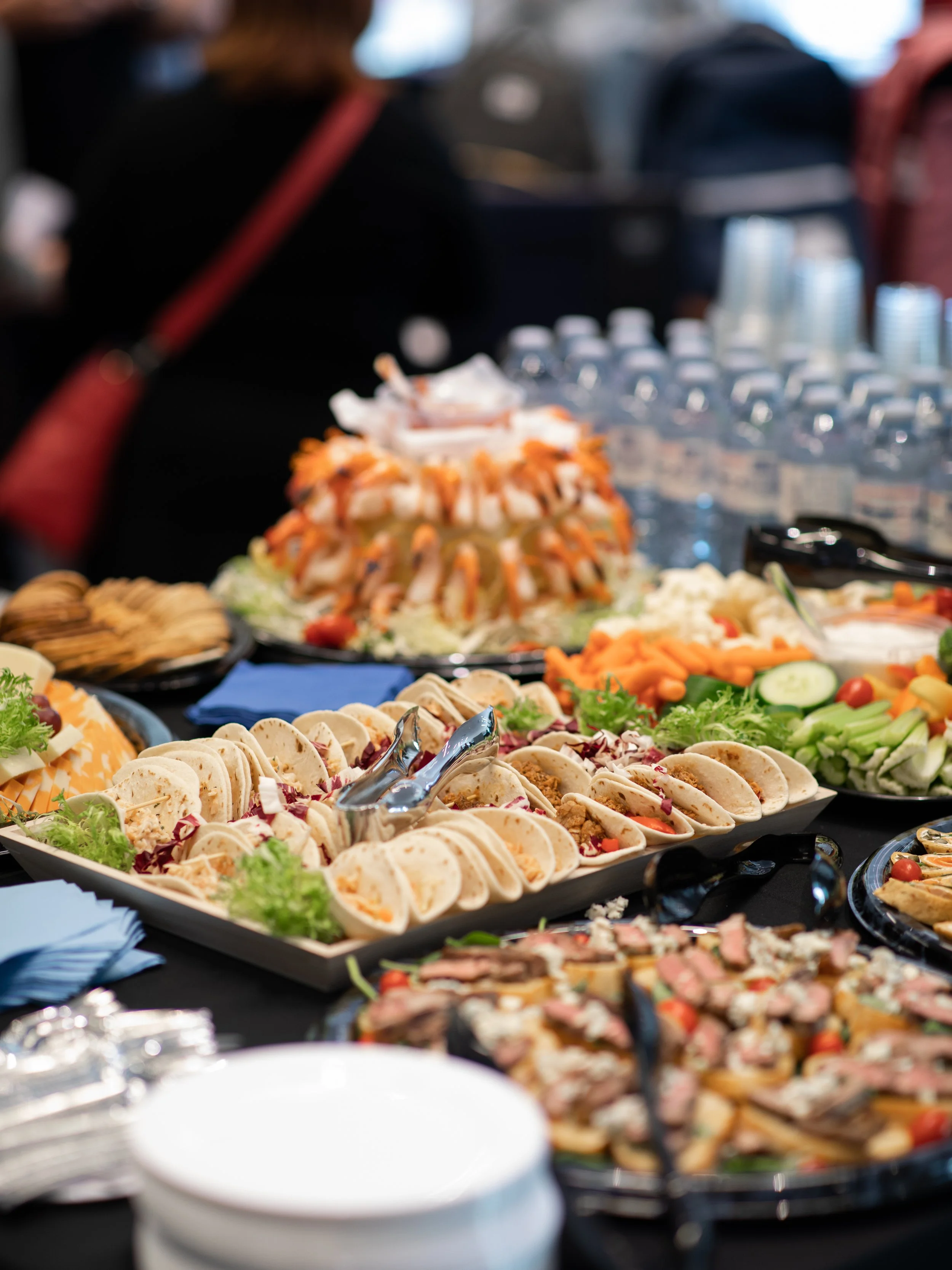 Buffet table with appetizers, vegetables, chips, dip, and a cake in the background.