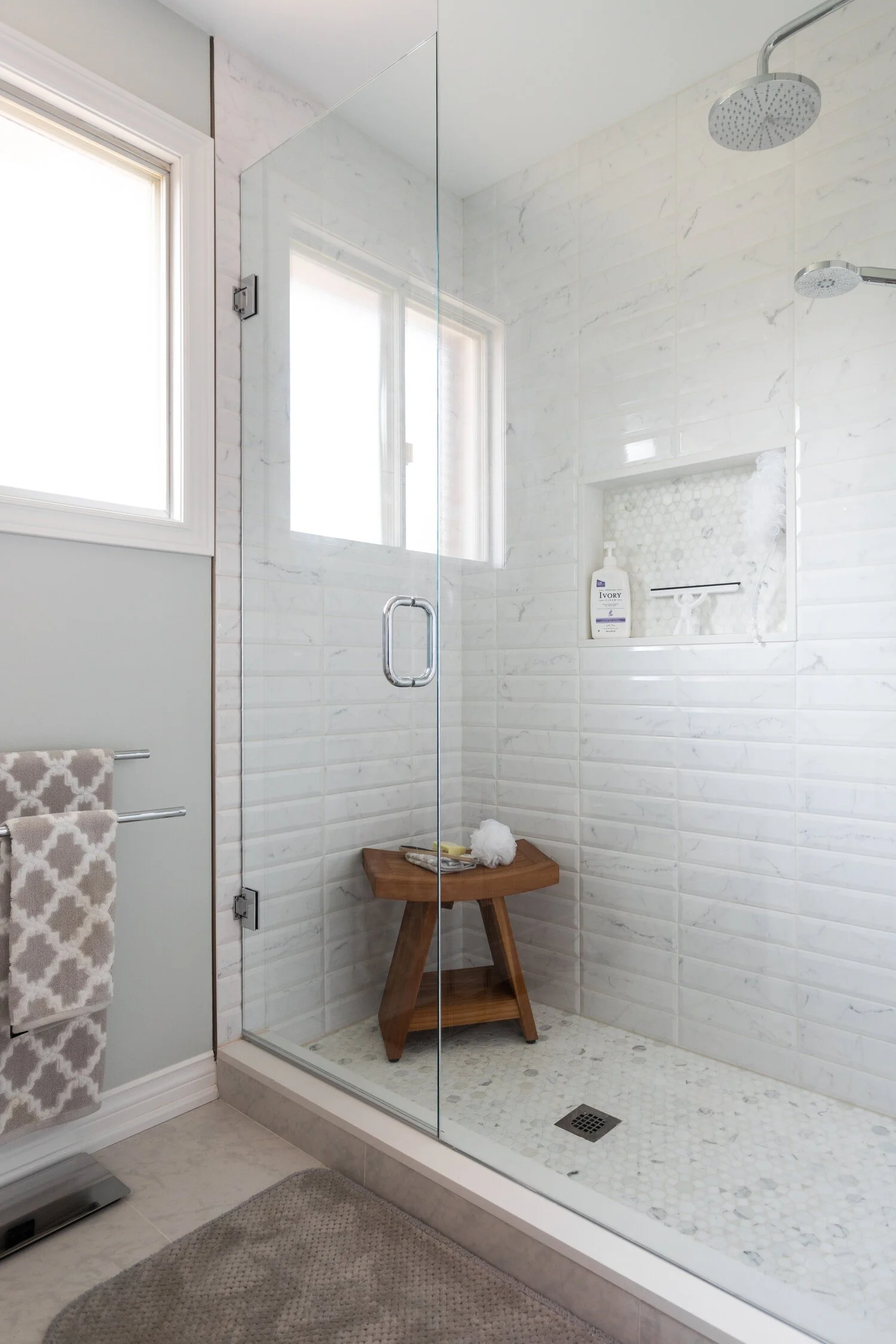 Bathroom shower with marble tile, glass door, and neatly styled accessories.