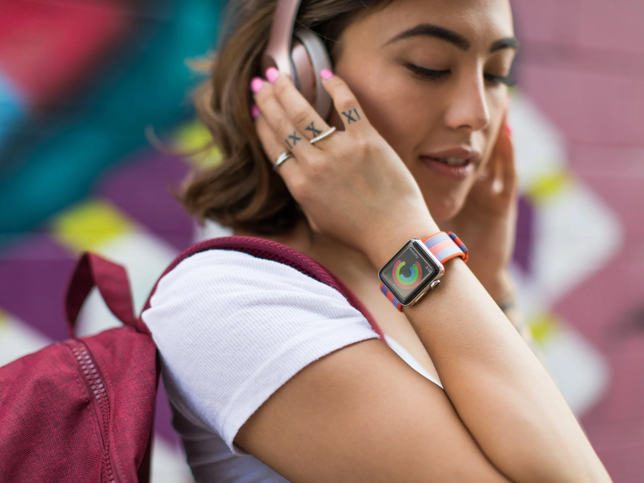Young woman wearing headphones and a smartwatch, looking down and smiling.