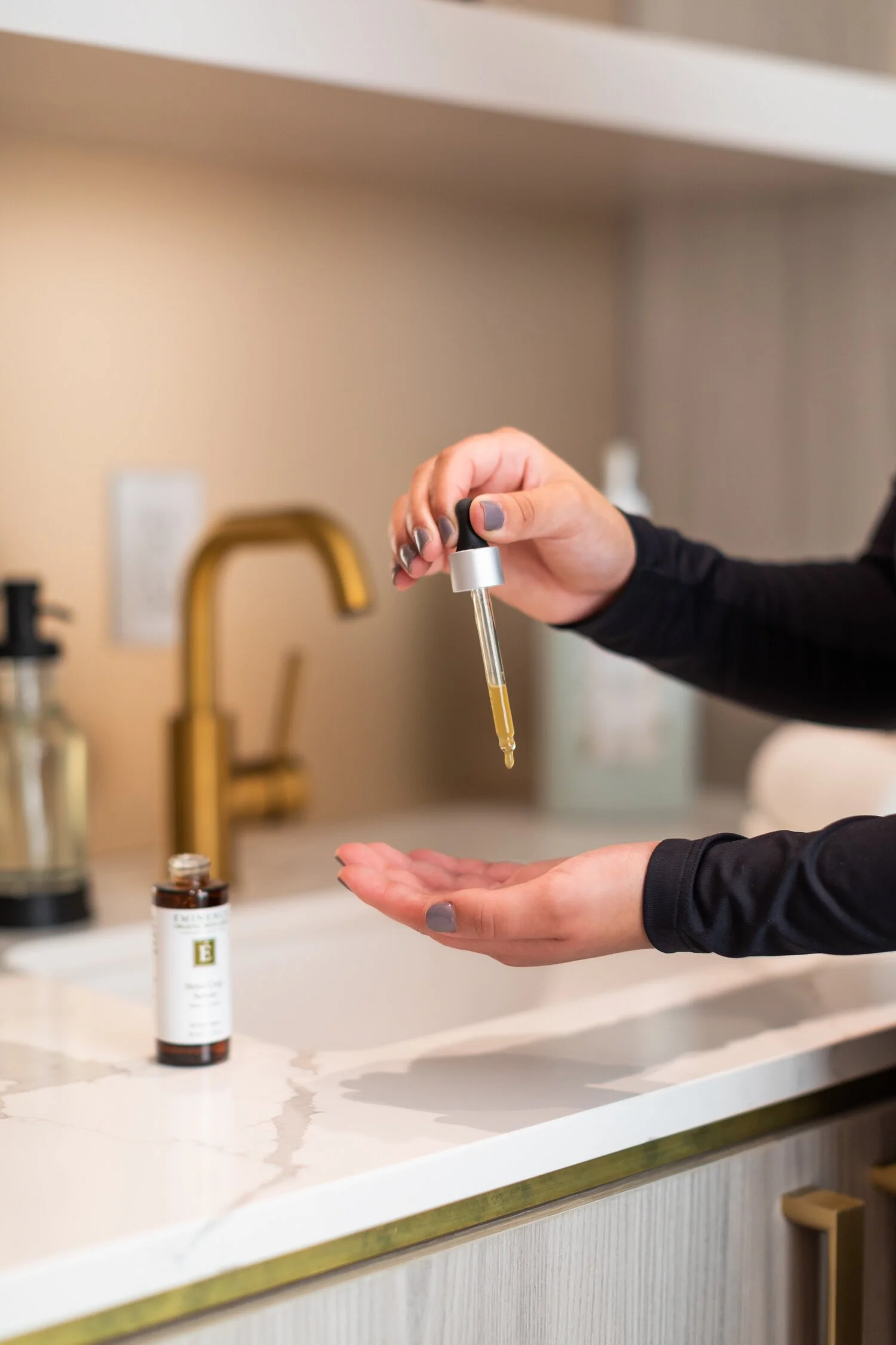 Person dispensing liquid from a dropper onto their hand in a kitchen.